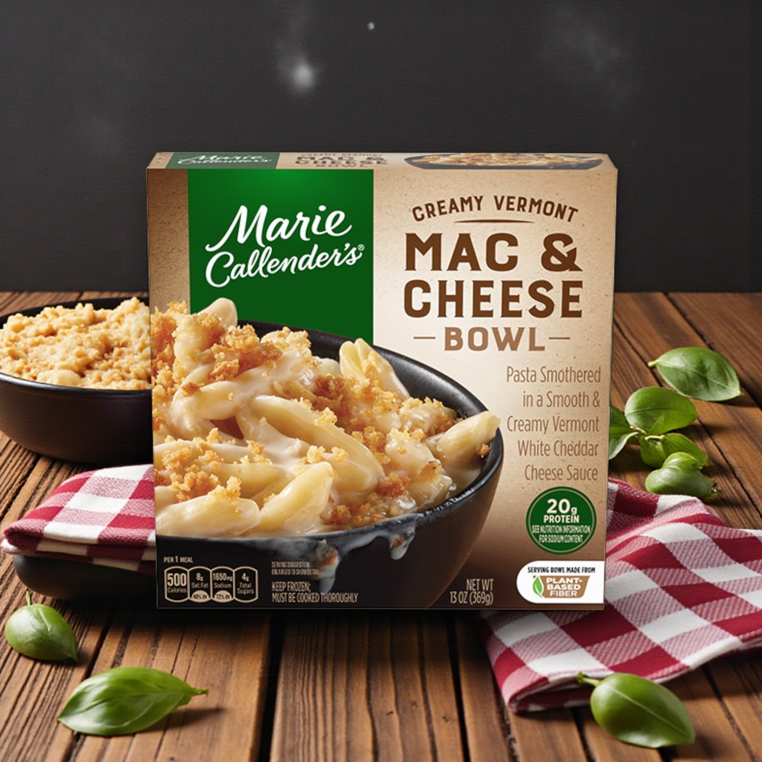 Marie Callender’s Comfort Classics Entrée Combo – 5 Delicious Meals sits on a wooden surface with basil leaves, a red plaid napkin, and a bowl of mac and cheese in the background.