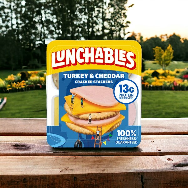 A package of Lunchables Turkey & Cheddar Cheese, 3.2 oz. - 1 Pack on a wooden table in an outdoor garden setting. This kid-friendly meal from Lunchables boasts 13g of protein per serving and 100% freshness guaranteed.