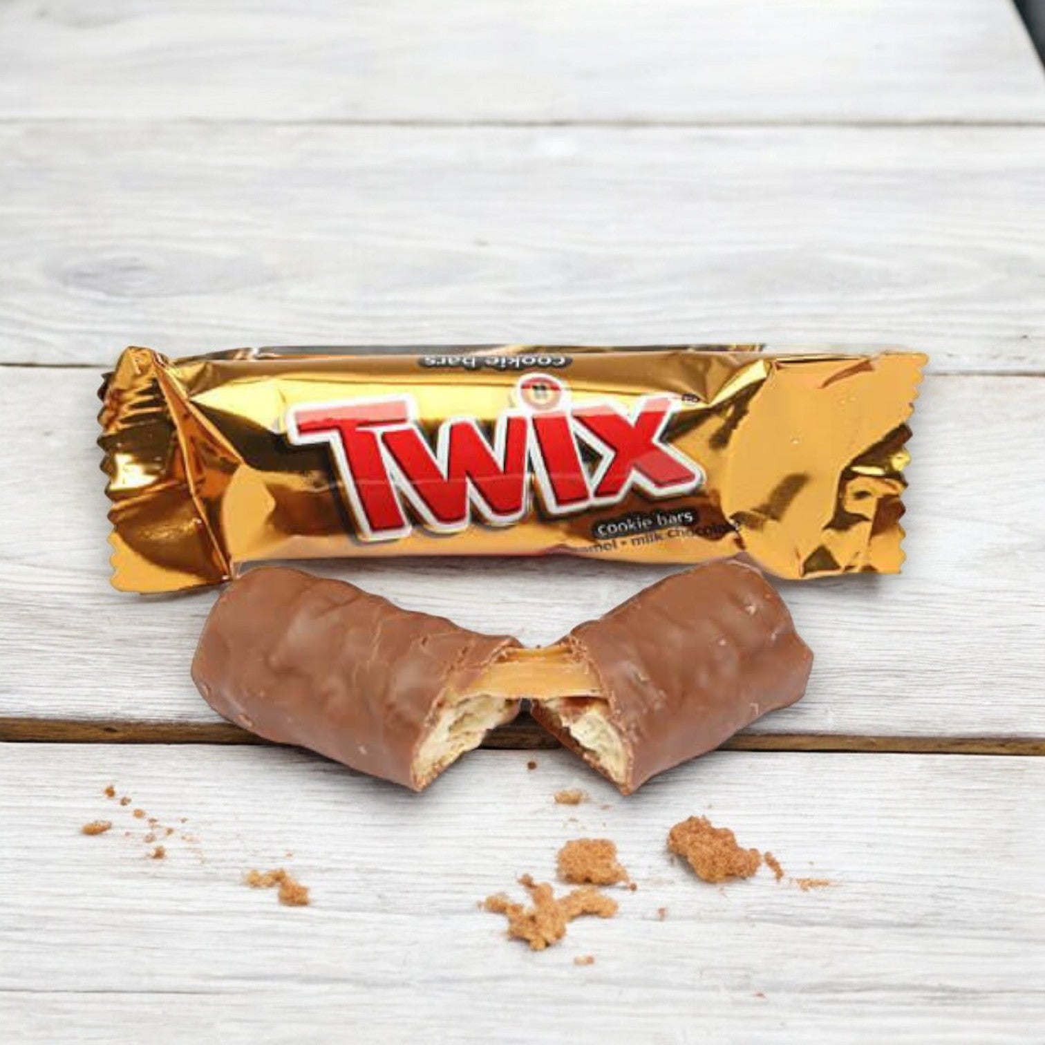 A Fun Size Twix bar from Mars, split in half with crumbs scattered around, placed on a wooden surface. The golden wrapper from the 5 Count Fun Size Bars pack is in the background.