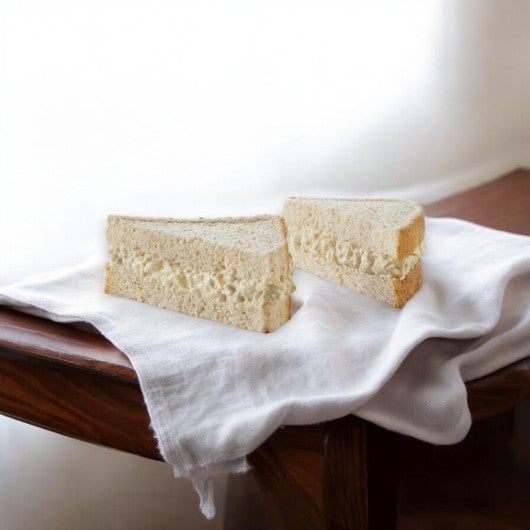 A sandwich cut in half, with an Albacore Tuna Salad filling, rests on a white cloth on a wooden surface.