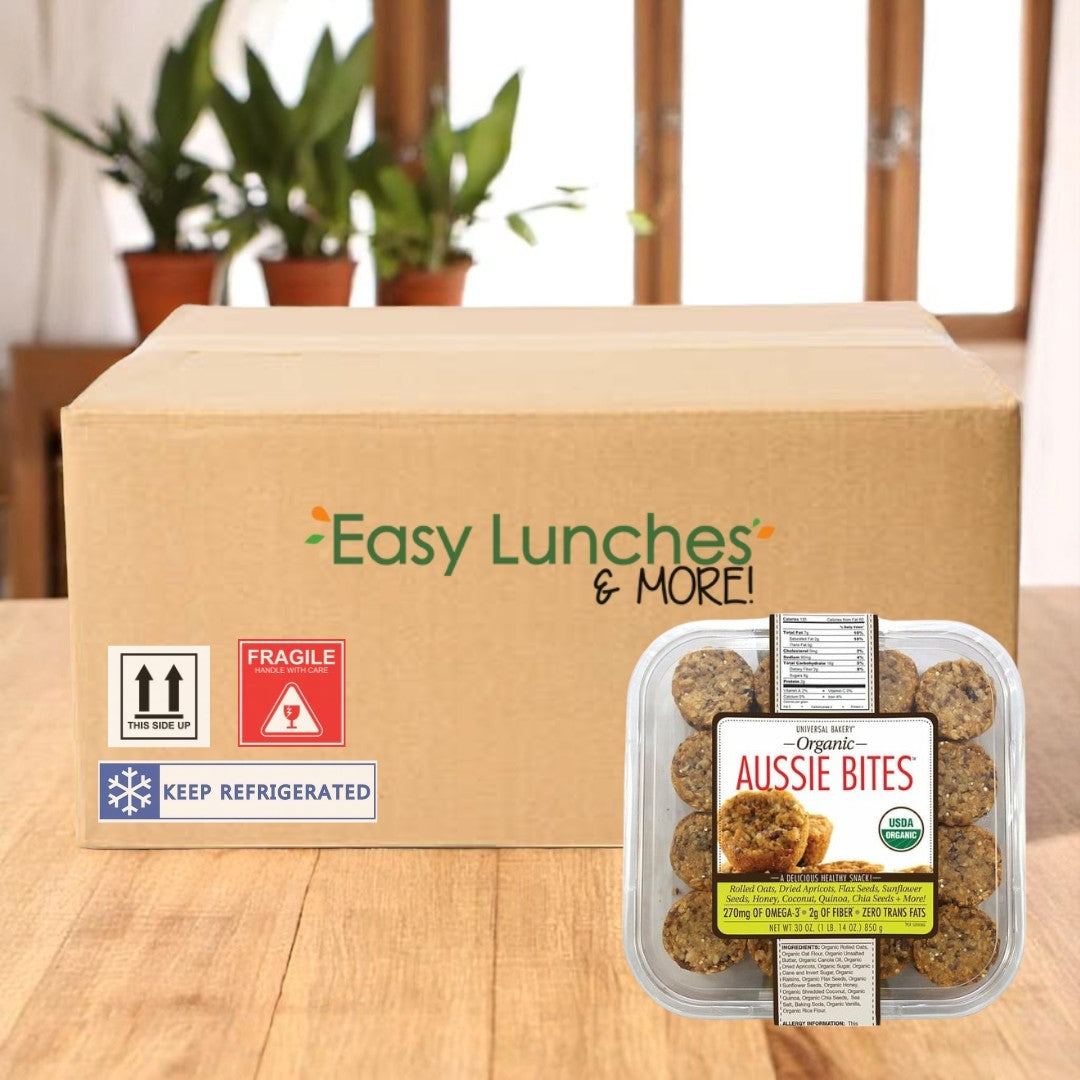 A box labeled "Easy Lunches & MORE!" sits on a table with Best Express Foods Inc Universal Bakery Organic Aussie Bites, 30 oz—1 Count, highlighting their nutritional benefits; plant pots are in the background.