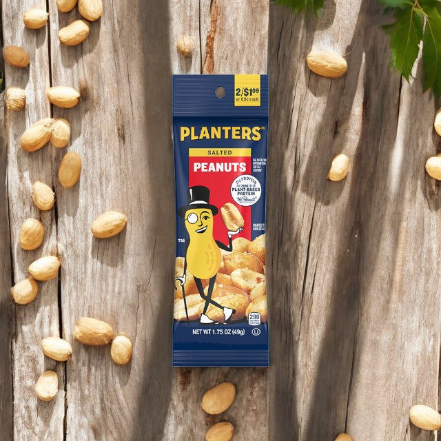 A packet of Planters Peanuts from a 5-bag pack, each weighing 1.5 oz, rests on a wooden surface with scattered roasted peanuts around it. The packaging features a cartoon peanut wearing a top hat and monocle.