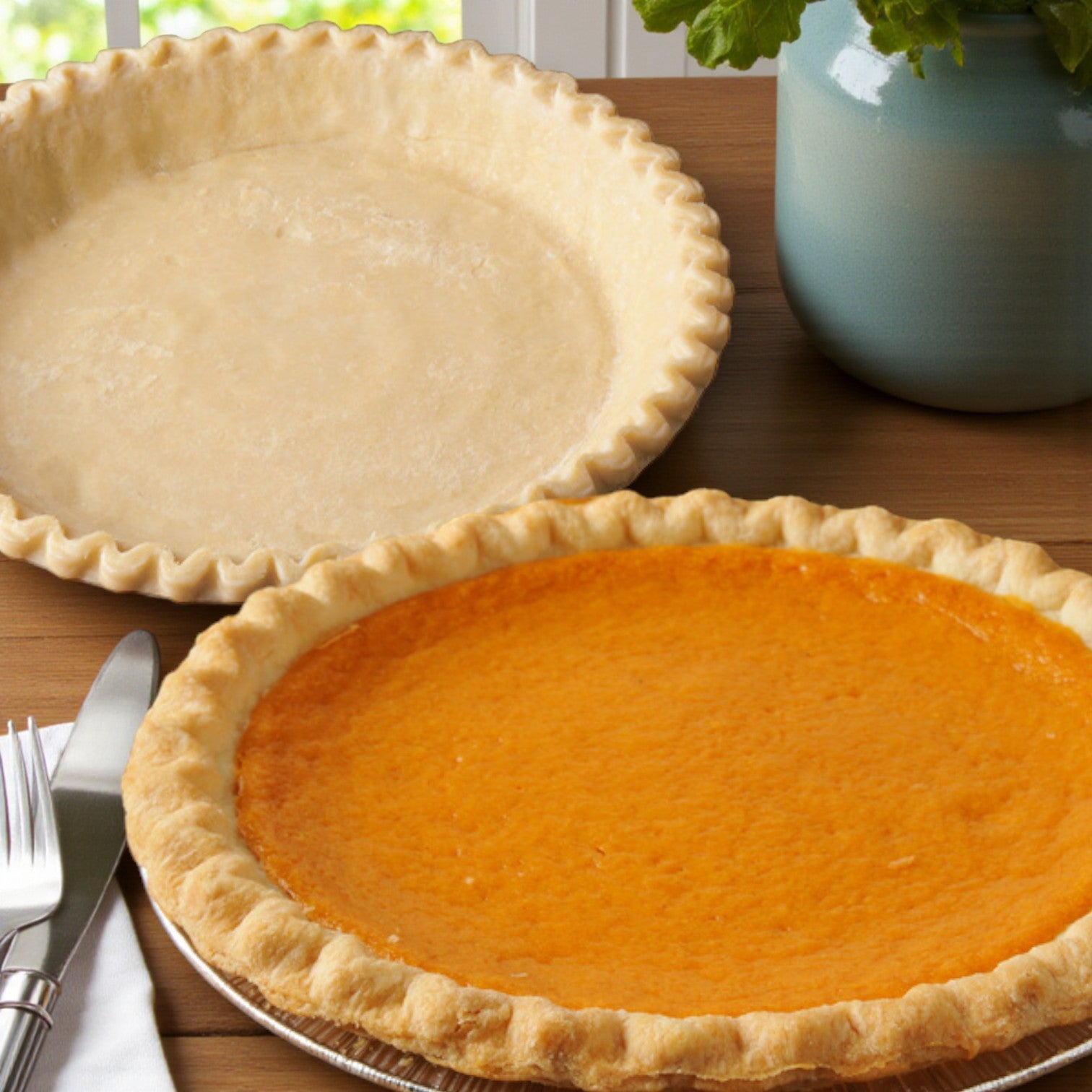 Two Sysco Classic Ready-to-Bake 10" All-Vegetable Pie Shells (20/8 oz) sit on a wooden surface—one unbaked and empty, the other baked with orange filling. A potted plant and utensils are nearby.