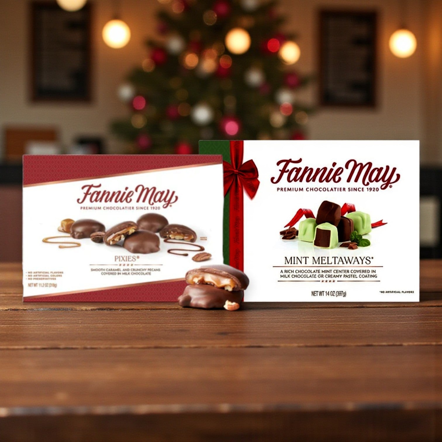 Two Fannie May Chocolate Combo Pack – Pixies & Mint Meltaways (2 Count) boxes from Fannie May sit on a wooden table with assorted chocolates in front, set against a softly blurred café backdrop for an inviting display.