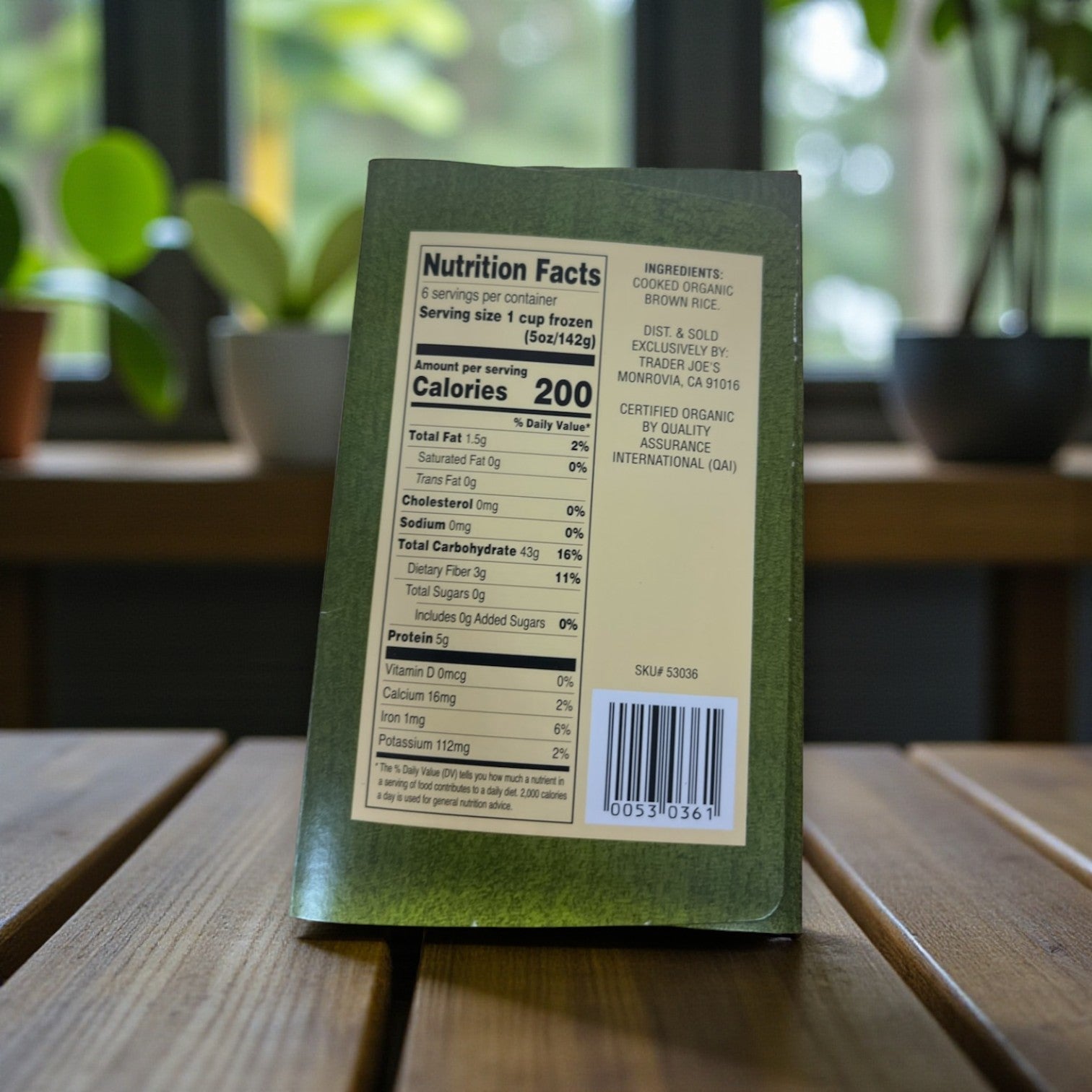 A green Easy Lunches package of Trader Joe’s Organic Brown Rice, 30 oz – 3 Pack, shows nutrition facts and ingredients on a wooden table with a blurred outdoor background—ideal for quick, microwave-ready rice meals.