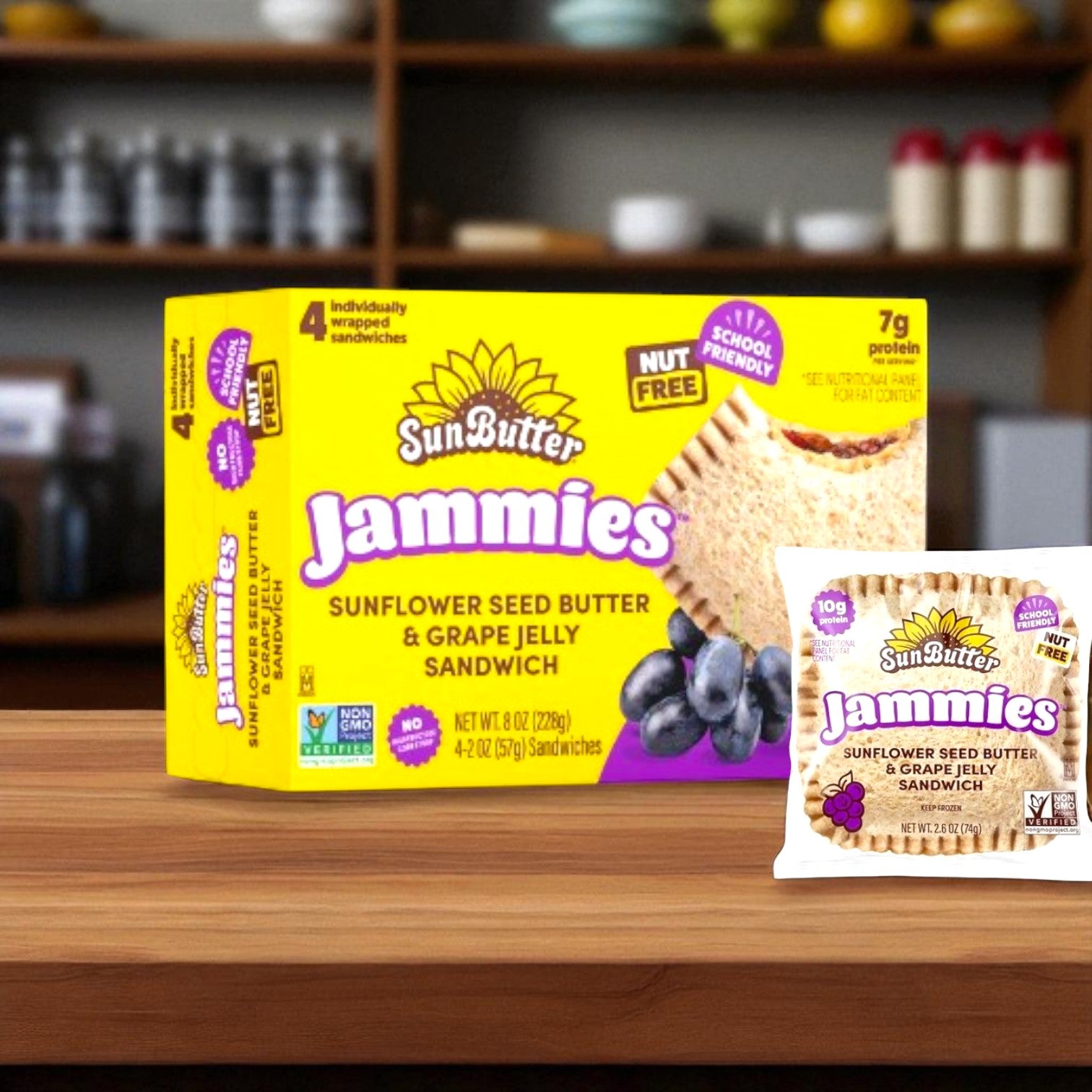 A box and single serving of SunButter Sunflower Seed Butter & Grape Jelly Sandwich, 8 oz - 4 Count by SunButter are shown on a wooden counter with a blurred kitchen shelf in the background, highlighting these nut-free snacks.
